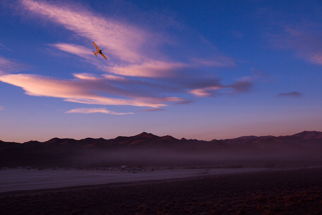 Airplane flies over mountain range in Nevada desert against sky at dusk