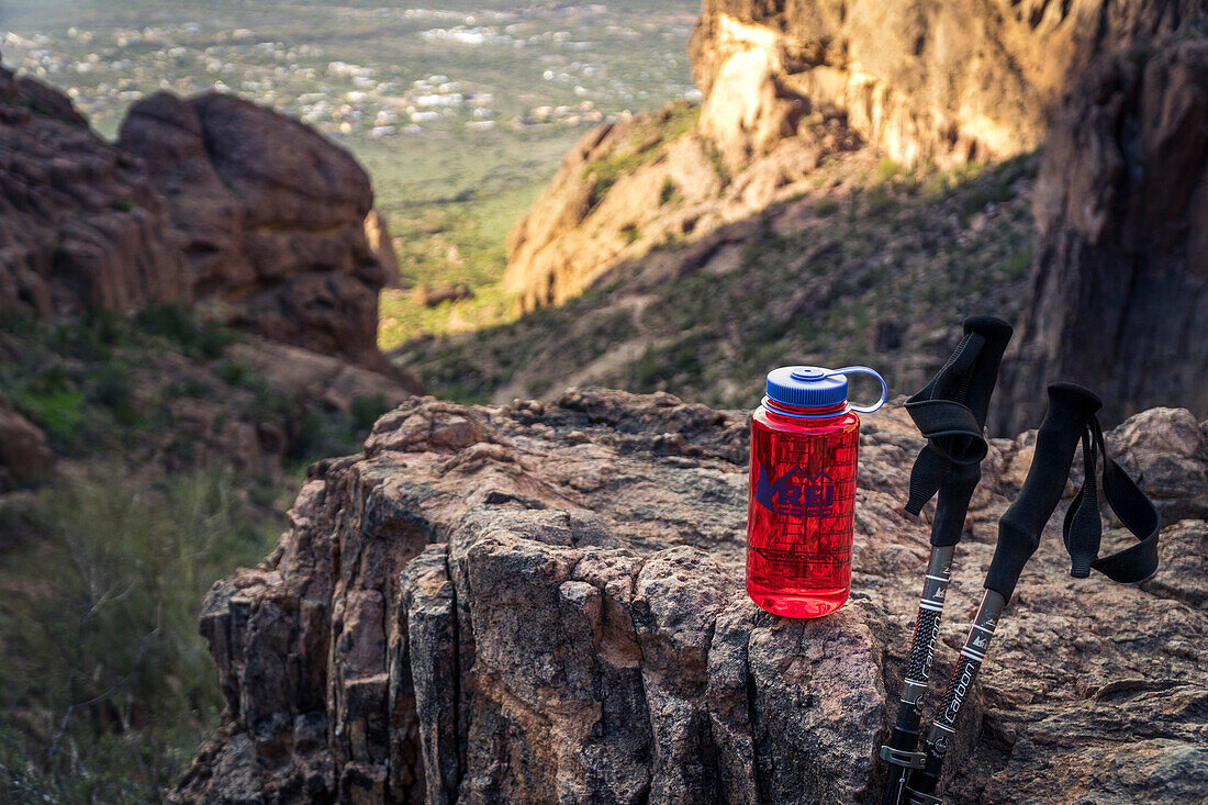 Rote Wasserflasche mit zwei Wanderstöcken auf Felsen, Aberglaube-Berge, Arizona, USA