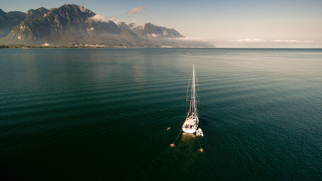 Segelboot verankert im Geneva See in Waadt-Kanton an einem schönen Tag mit Bergen im Hintergrund und im blauen Himmel.