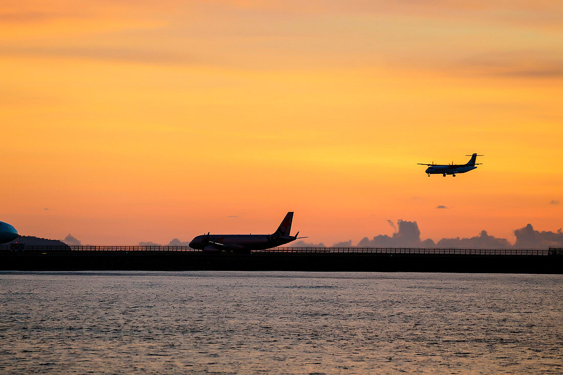 Silhouettes of aircraft on the runway and another landing