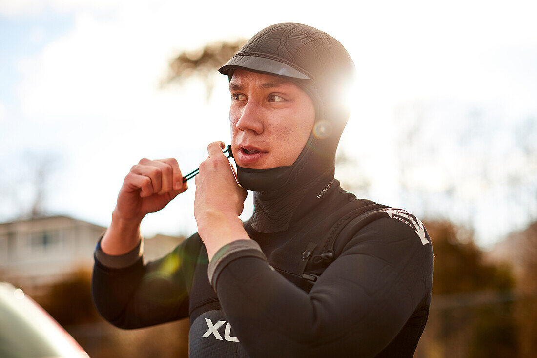 A surfer putting on his wetsuit hood