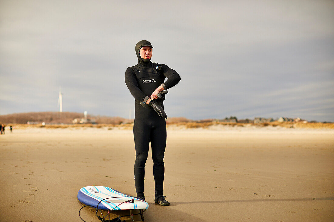 Ein Surfer setzen auf seine kalten Wetter-Handschuhe am Strand