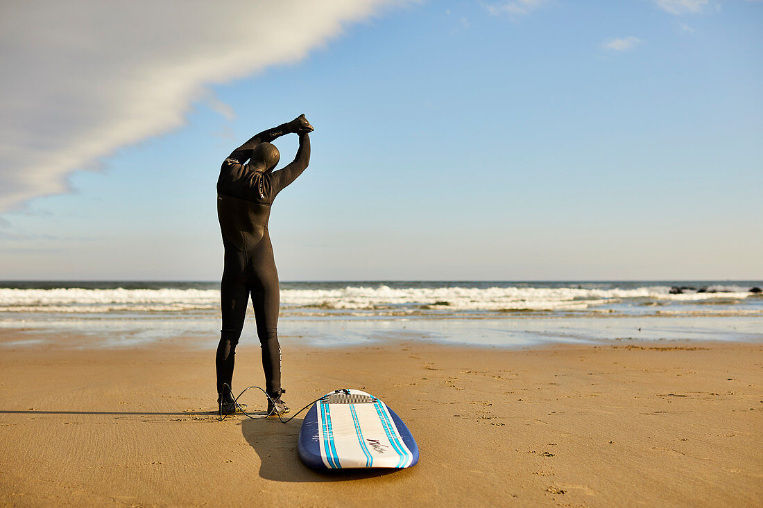 A male surfer stretching and warming up on the beach before surfing