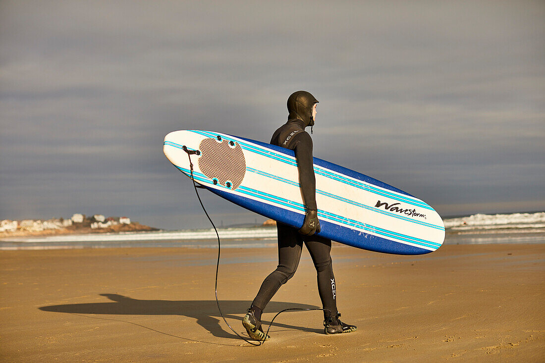 A surfer walking with his surfboard at Good Harbor Beach in Gloucester, Massachusetts