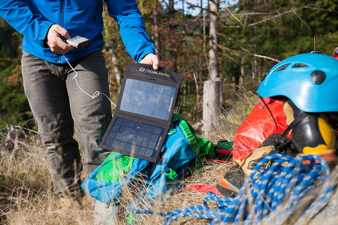 A climber uses a portable solar panel to charge a battery pack during a climbing trip