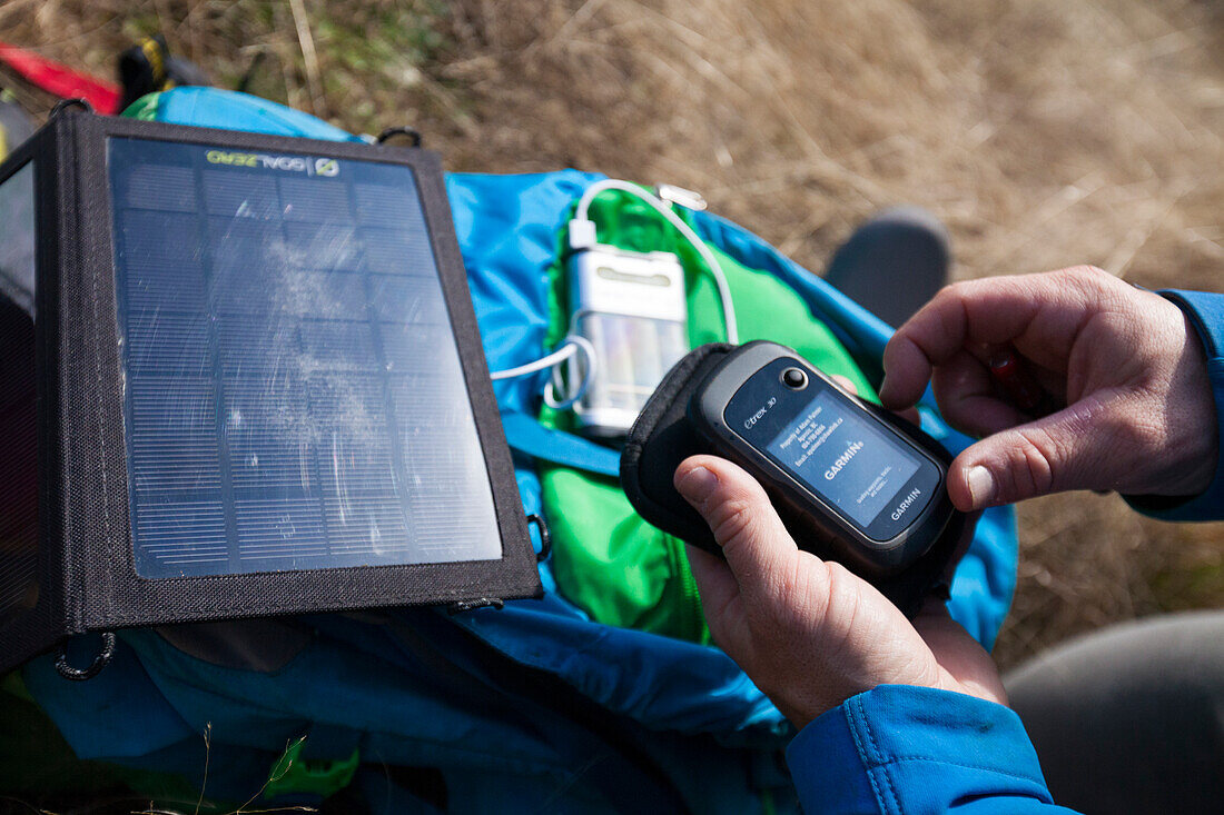 Ein Kletterer benutzt ein tragbares Solarpanel, um sein GPS während eines Kletterausflugs aufzuladen
