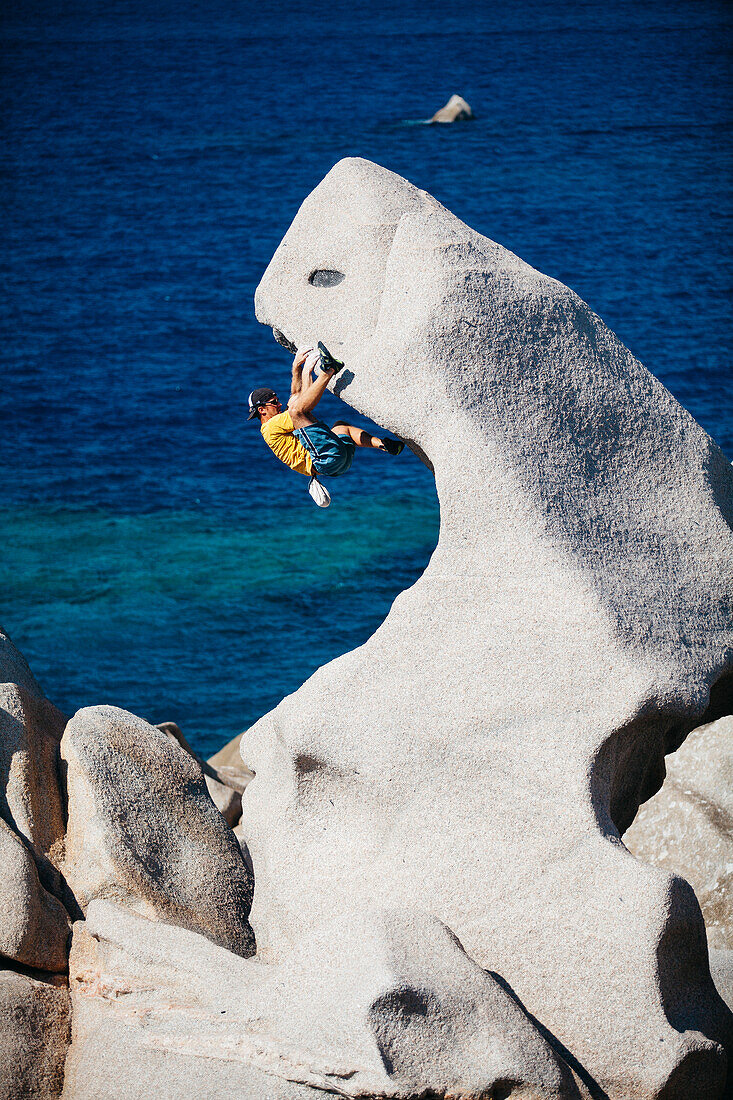 Bemannen Sie das Klettern auf Felsen nahe Meer, Capo Testa, Sardinien, Italien