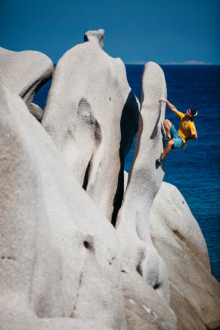Bemannen Sie das Klettern auf Felsen nahe Meer, Capo Testa, Sardinien, Italien