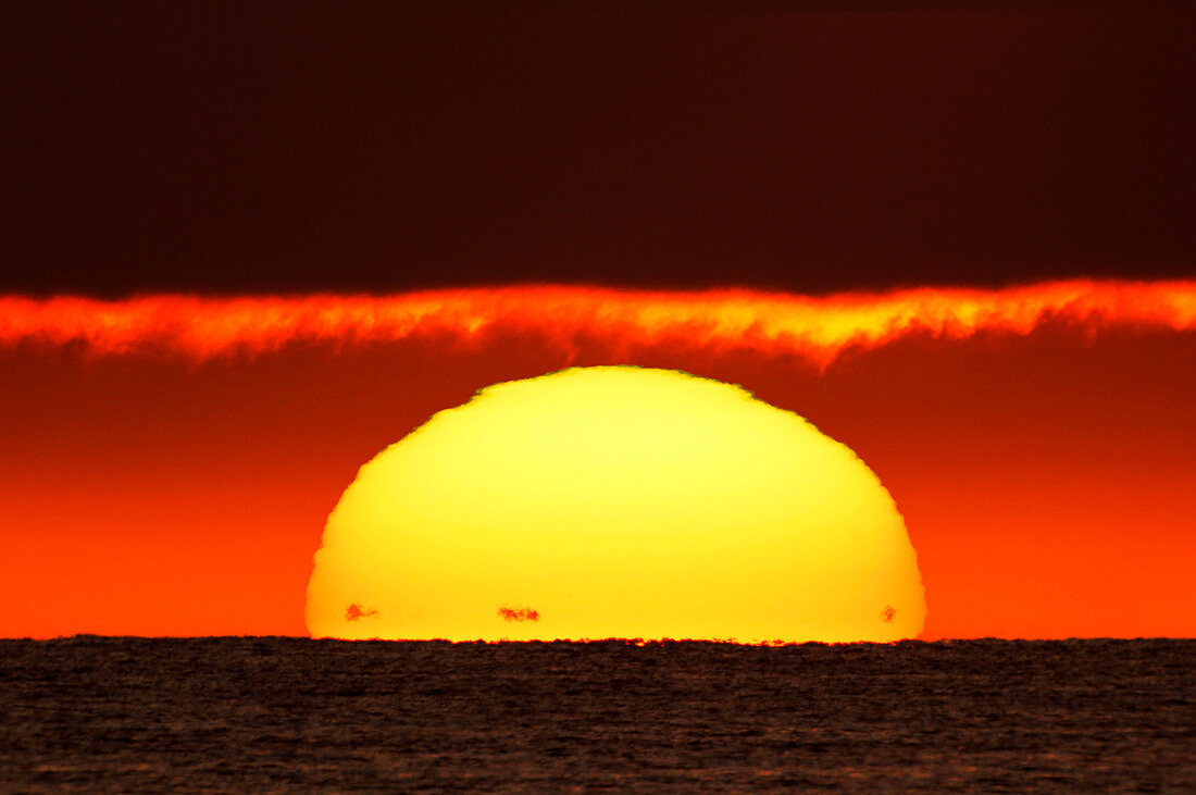 Frankreich, Normandie. Montmartin-sur-Mer, Sonnenuntergang. Die schwarzen Punkte am Fuß der Sonne sind die Küsten von Jersey