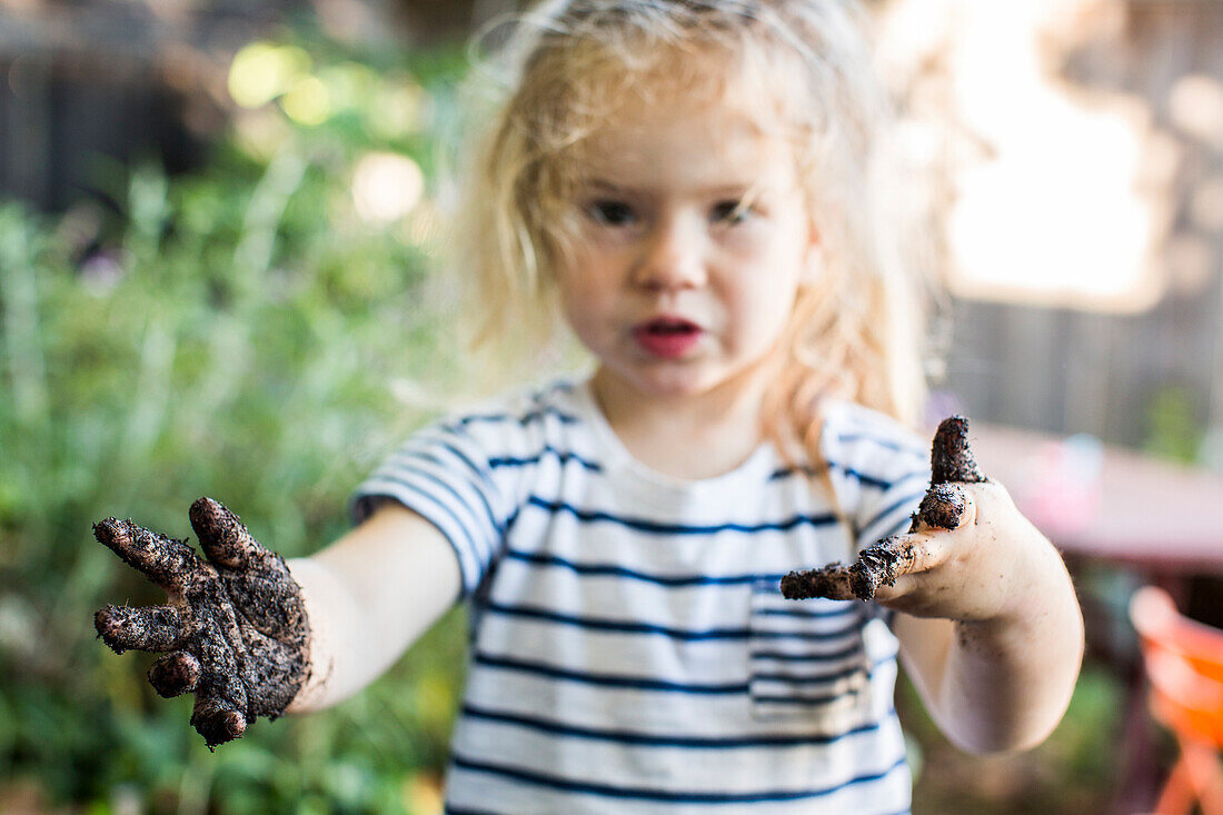 Caucasian girl with muddy hands in garden