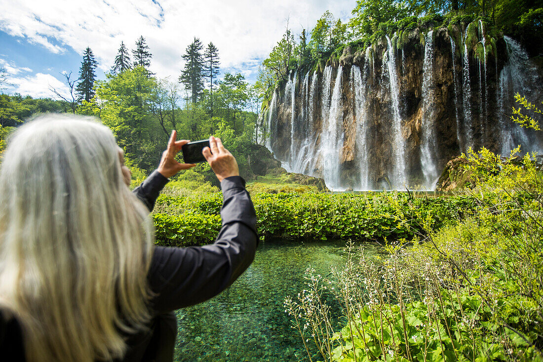 Older Caucasian woman photographing waterfall with cell phone