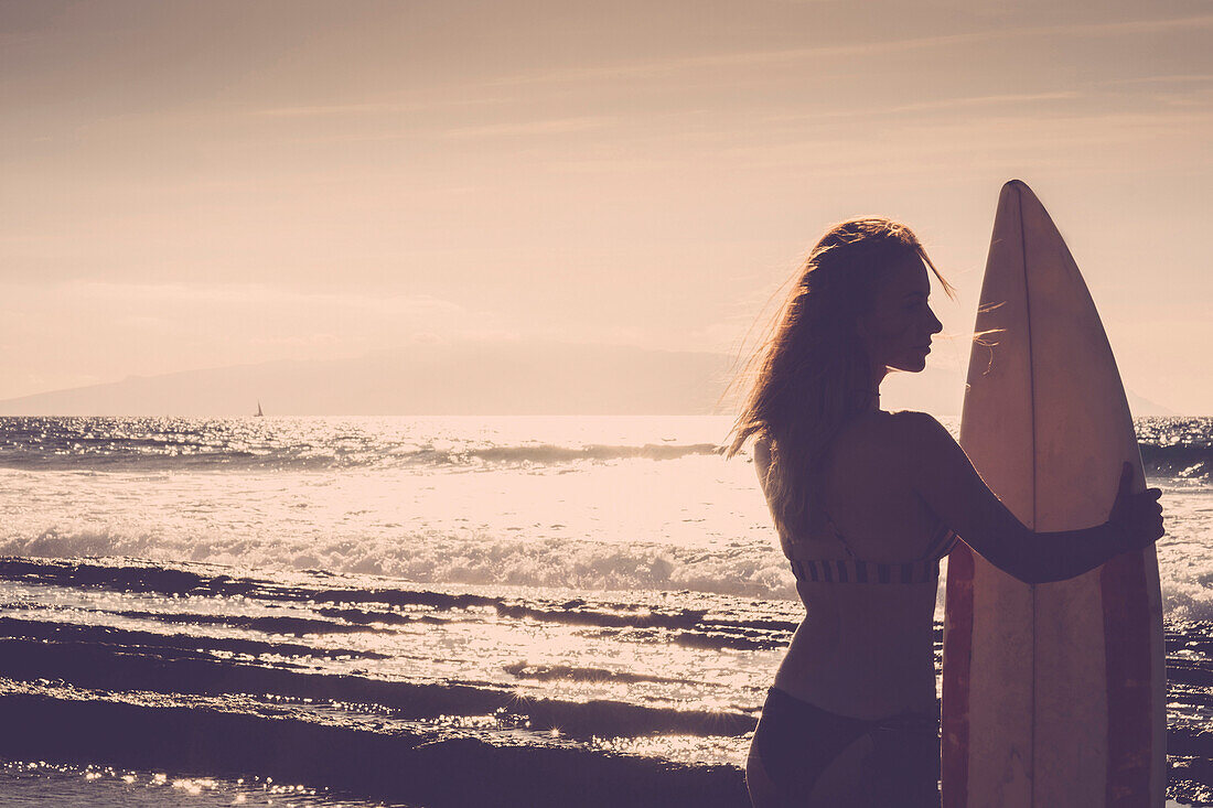 Caucasian woman standing on beach holding surfboard