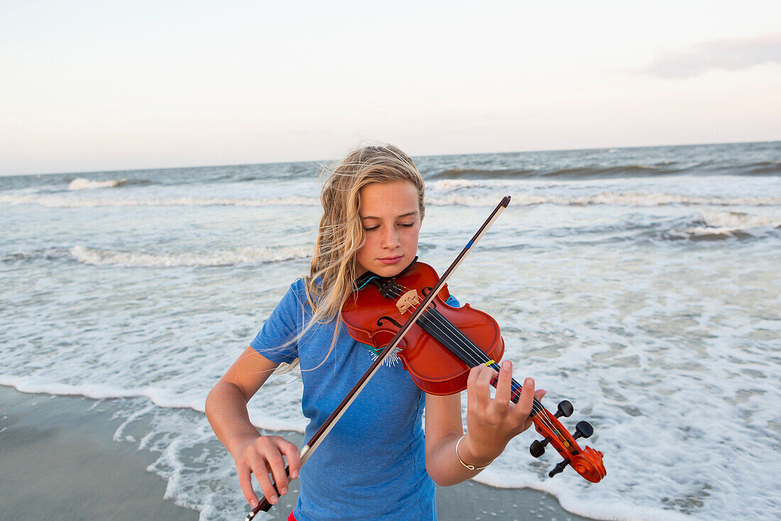 Caucasian girl playing violin at beach