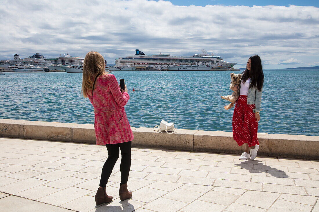 Junge Frau macht Selfie von Freundin mit Hund auf Arm beim Bummel entlang der Strandpromenade, Split, Split-Dalmatien, Kroatien, Europa