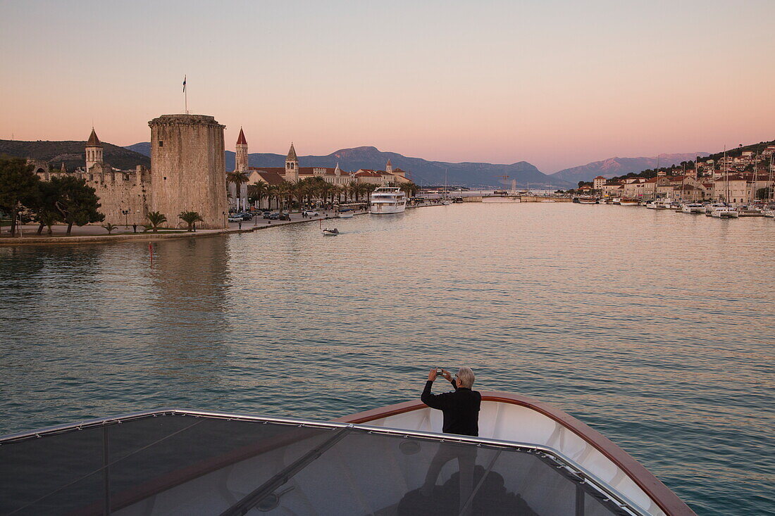 Man photographs Kamerlengo Castle and Old Town from bow of cruise ship MS Romantic Star (Reisebüro Mittelthurgau) at dusk, Trogir, Split-Dalmatia, Croatia