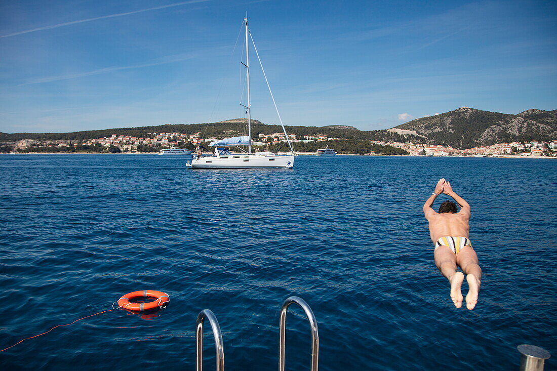 Mann springt von der Badeplattform von Kreuzfahrtschiff MS Romantic Star (Reisebüro Mittelthurgau) in die Adria mit Segelboot dahinter, nahe Hvar, Split-Dalmatien, Kroatien, Europa