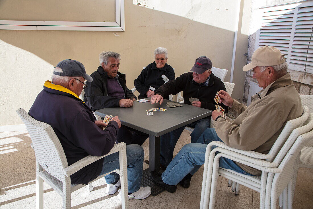 Fünf ältere Männer spielen Karten während sie auf Plastikstühlen vor einer Bar sitzen, Korcula, Dubrovnik-Neretva, Kroatien, Europa