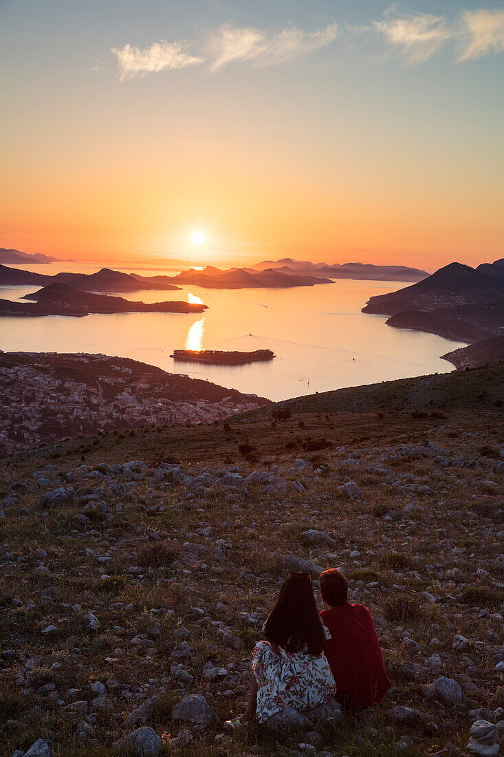 Paar genießt Aussicht über die Lapad-Halbinsel und vorgelagerte Inseln, vom Hügel nahe der Bergstatation der Dubrovnik-Gondel bei Sonnenuntergang aus gesehen, Dubrovnik, Dubrovnik-Neretva, Kroatien, Europa