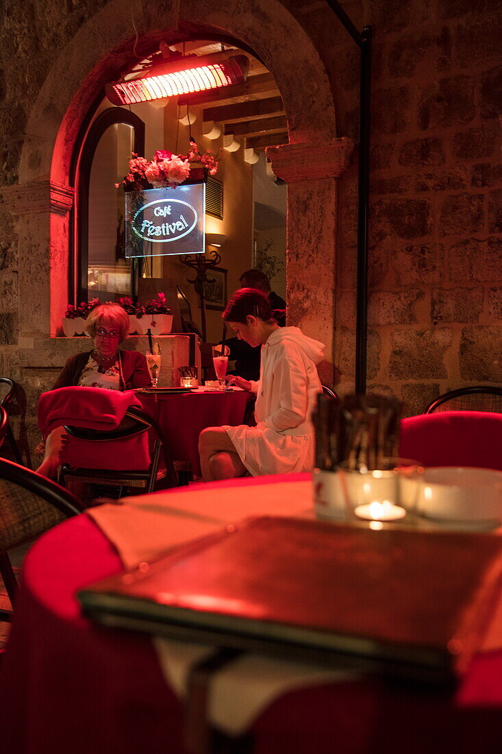 Mother and daughter sit outside cafe in Old Town and look at smartphones at night, Dubrovnik, Dubrovnik-Neretva, Croatia