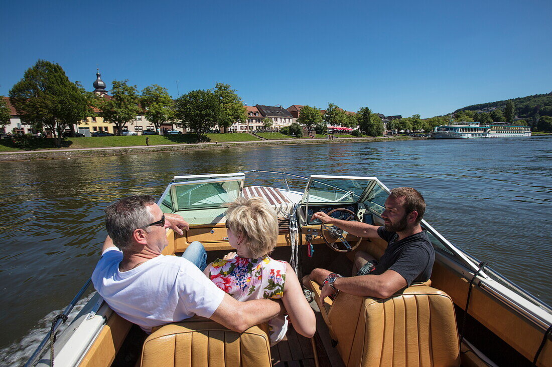 People enjoy motor boat excursion along Main river with river cruise ship Swiss Crown (Phoenix Kreuzfahrten) in distance, Marktheidenfeld, Spessart-Mainland, Franconia, Bavaria, Germany