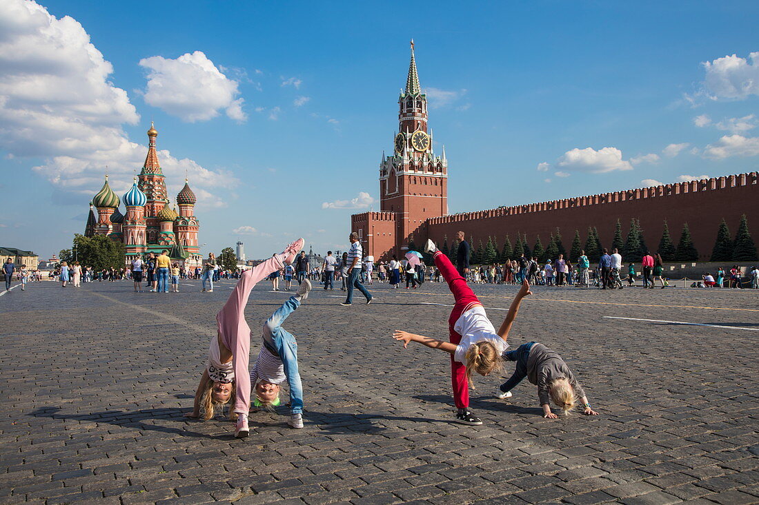 Junge Kinder spielen und schlagen Räder am Roten Platz mit Basilius-Kathedrale und Moskauer Kremlmauer dahinter, Moskau, Russland, Europa