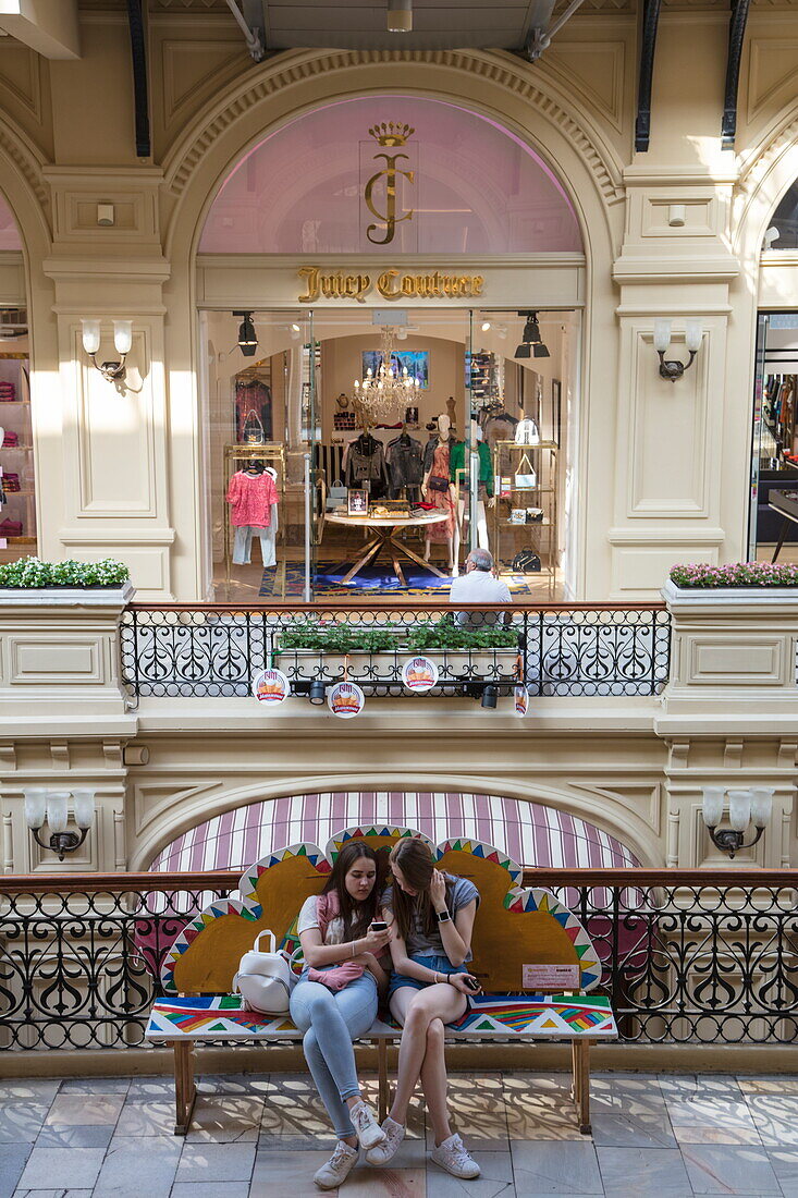 Zwei Teenager blicken auf ihr Smartphone im GUM Kaufhaus am Roten Platz, Moskau, Russland, Europa