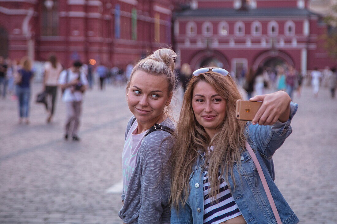 Two young women take selfie photograph with iPhone in Red Square, Moscow, Russia