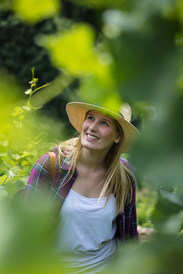 Young woman with sun hat walks through vines at Iphöfer Julius-Echter-Berg vineyard, Iphofen, Franconia, Bavaria, Germany