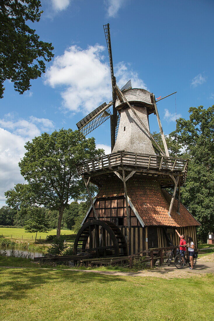 Couple with bicycles in front of Hüvener Mühle combination windmill and watermill, near Hüven, Emsland, Lower Saxony, Germany
