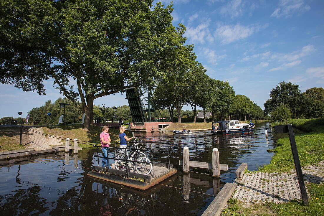 Couple with bicycles take rope ferry across canal, Klazienaveen, Drenthe, Netherlands