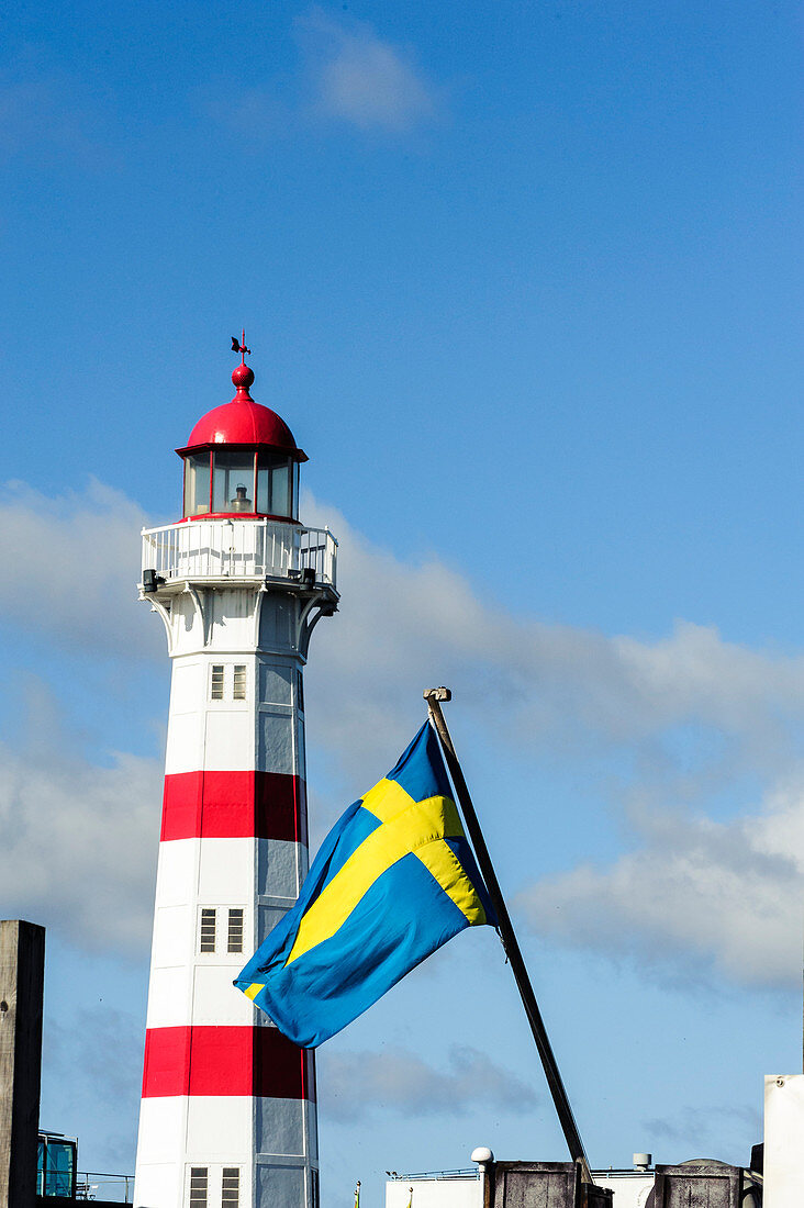 Rot weißer Leuchtturm im sarniertem Hafengebiet mit schwedischer Flagge davor, Malmö, Südschweden, Schweden