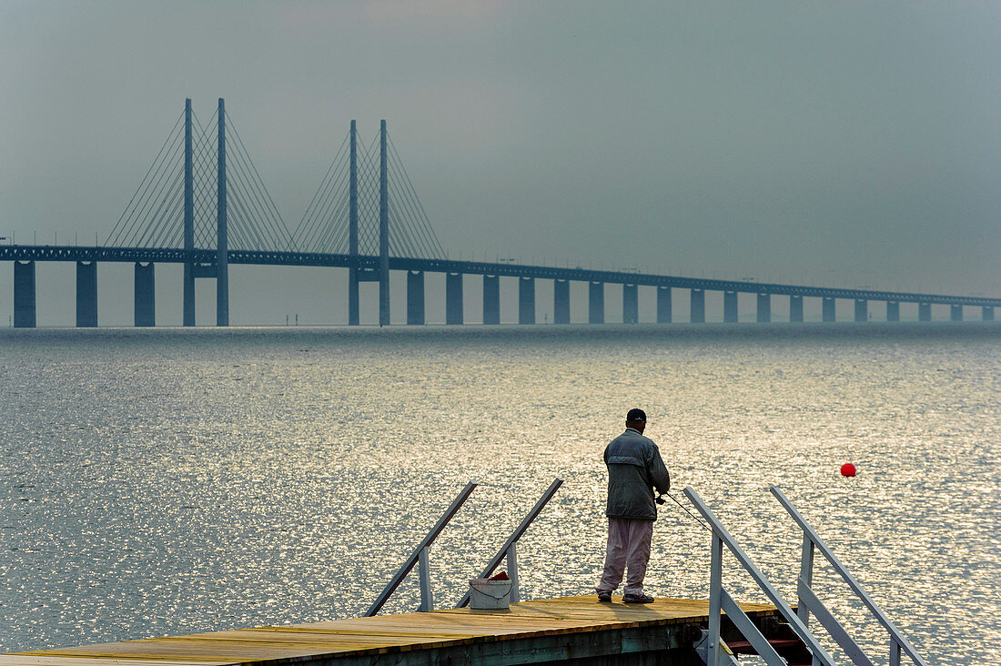 Gewitterstimmung über der Öresundbrücke und Sonne strahlt auf das Meer, Mann angel auf einem Bootssteg, Oresundbrücke, Malmö, Südschweden, Schweden