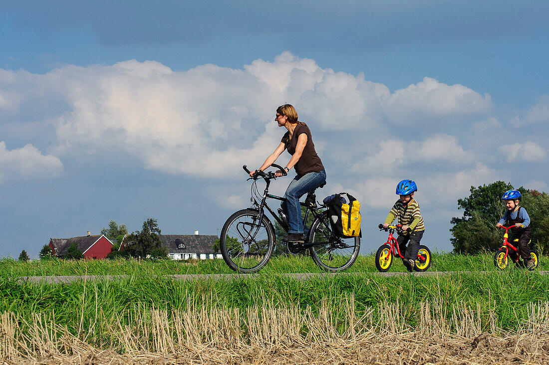 Mutter fährt Fahrrad und Kinder mit Laufrädern auf der Insel Ven, Skane, Südschweden, Schweden