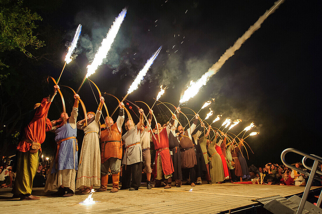 Menschen in Kostuemen machen Feuershow mit Bogenschießen und Feuerpfeile, mittelalterliches Fest, Eroeffnugsfeier , Schweden