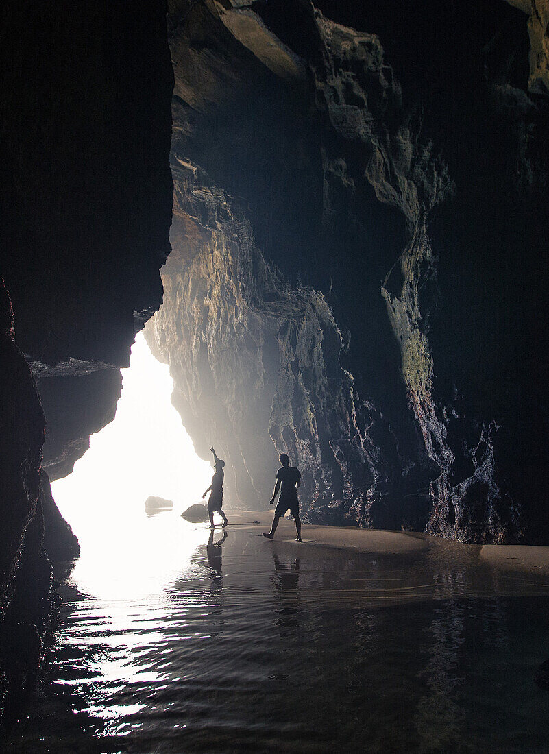 Two young men walking through a cave at the beach Praia da Amoreira,  Aljezur, Faro, Portugal