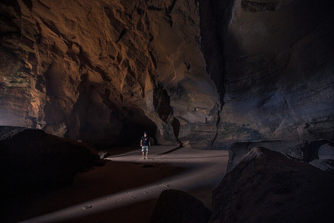 Young man walking through a cave at the beach Praia da Amoreira,  Aljezur, Faro, Portugal