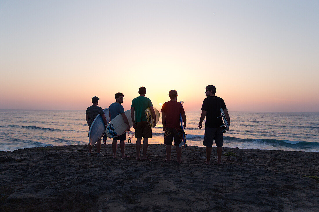 Five young surfer standing at the beach Praia da Amoreira at sunset,  Aljezur, Faro, Portugal