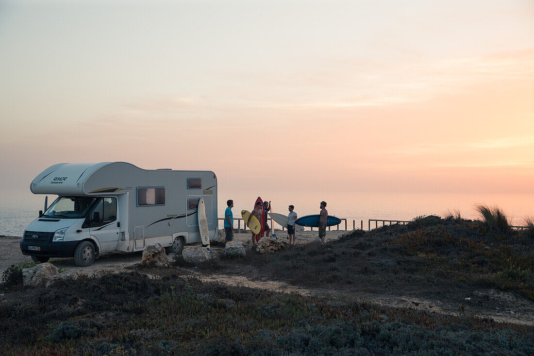 Fünf junge Surfer stehen an ihrem Wohnmobil am Strand Praia da Amoreira,  Aljezur, Faro, Portugal