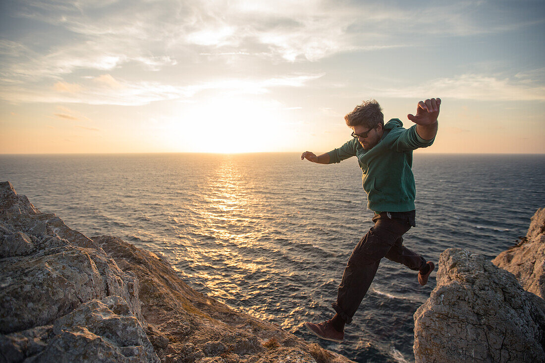Junger Mann springt auf einer Klippe am Strand Praia da Amoreira,  Aljezur, Faro, Portugal