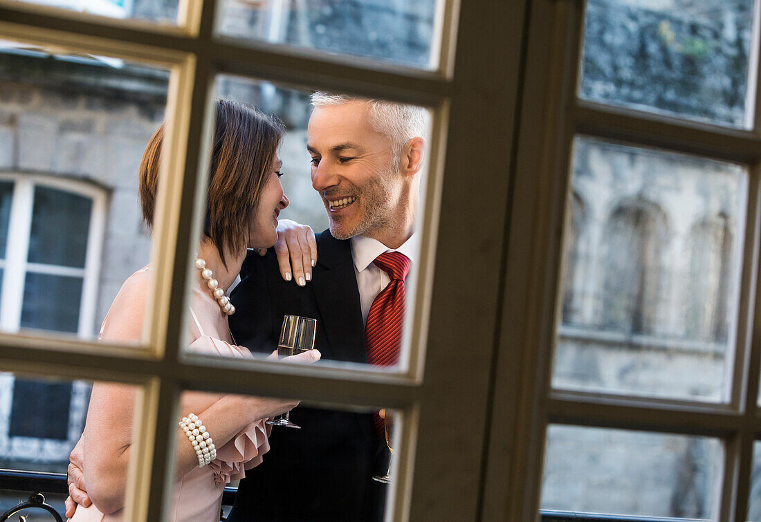 Well-dressed Caucasian couple drinking champagne behind window