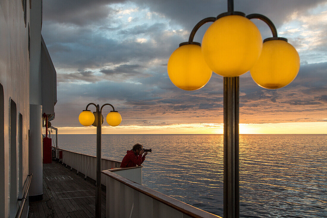 photographer on the ship's upper deck in front of a setting sun, astoria cruise ship by the icelandic coast, iceland