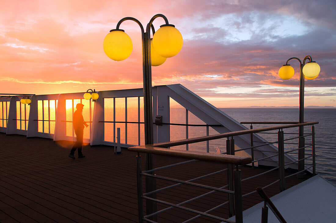 photographer on the ship's upper deck in front of a setting sun, astoria cruise ship by the icelandic coast, iceland