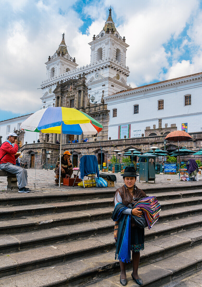 A traditionally dressed indigenous woman sells textiles in central Quito, Ecuador, South America