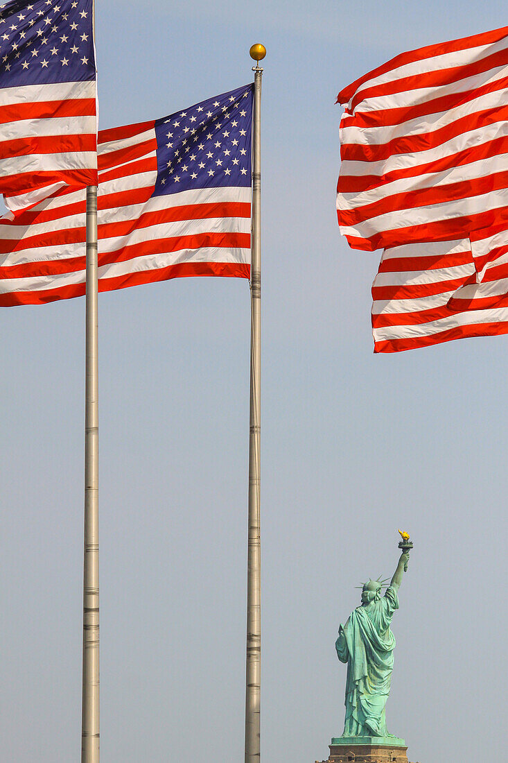 perspective of the statue of liberty with american flags in the foreground, new york harbor, new york city, state of new york, united states, usa