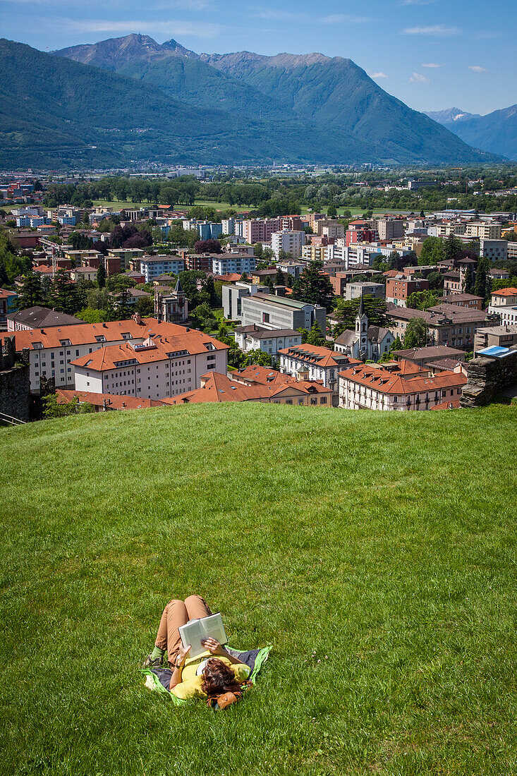 woman reading a book while lying on the lawn of montebello castle in bellinzona, listed as a world heritage site by unesco, bellinzona, canton of ticino, switzerland
