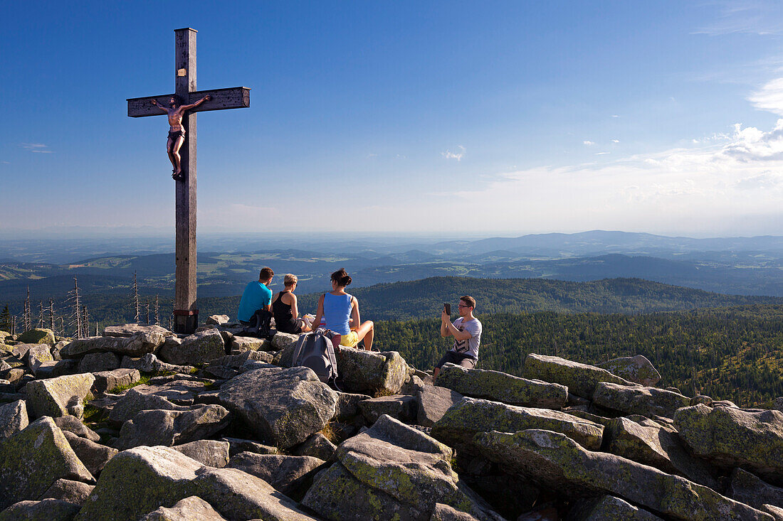 Hiker resting at the summit cross of the Lusen summit, Bavarian Forest, Bavaria, Germany