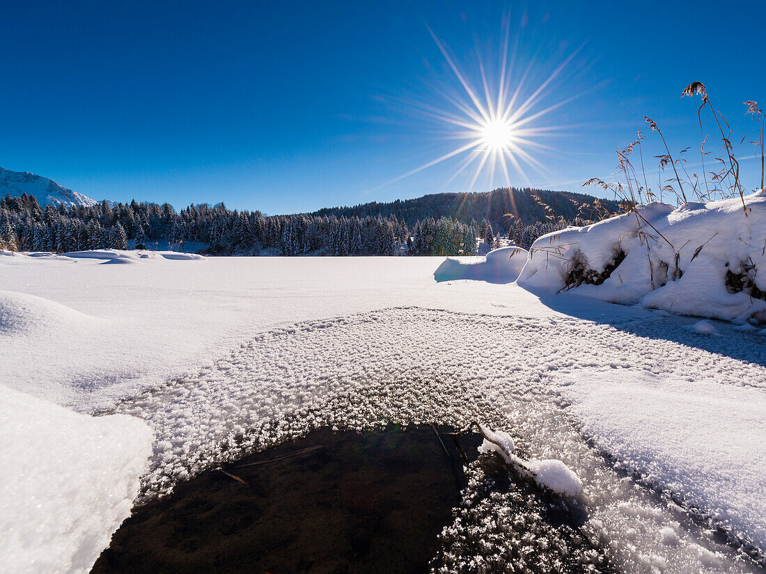 Neuschnee auf dem nahezu komplett gefrorenen Wagenbrüchsee in Bayern, Deutschland