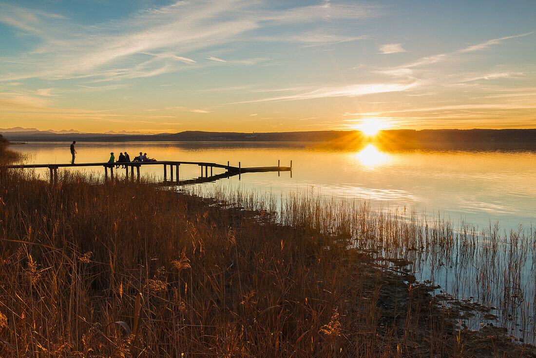 People enyoing the sunset on a jetty at lake Ammersee, Bavaria, Germany