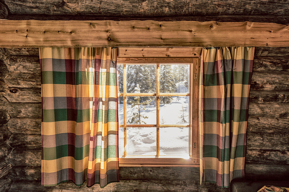 Blick aus dem Fenster einer gemütlichen Blockhütte hinaus in die Schneelandschaft, Luosto, finnisch Lappland
