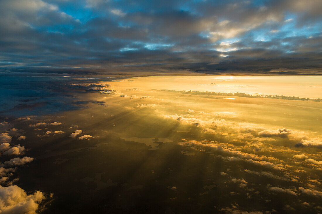 Die dünne Wolkendecke trennt den blauen Himmel vom warmen Licht der tief stehenden Sonne, Luftaufnahme